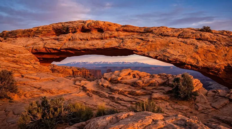 A red sandstone arch near Moab glowing orange at sunset with the La Sal mountains beyond