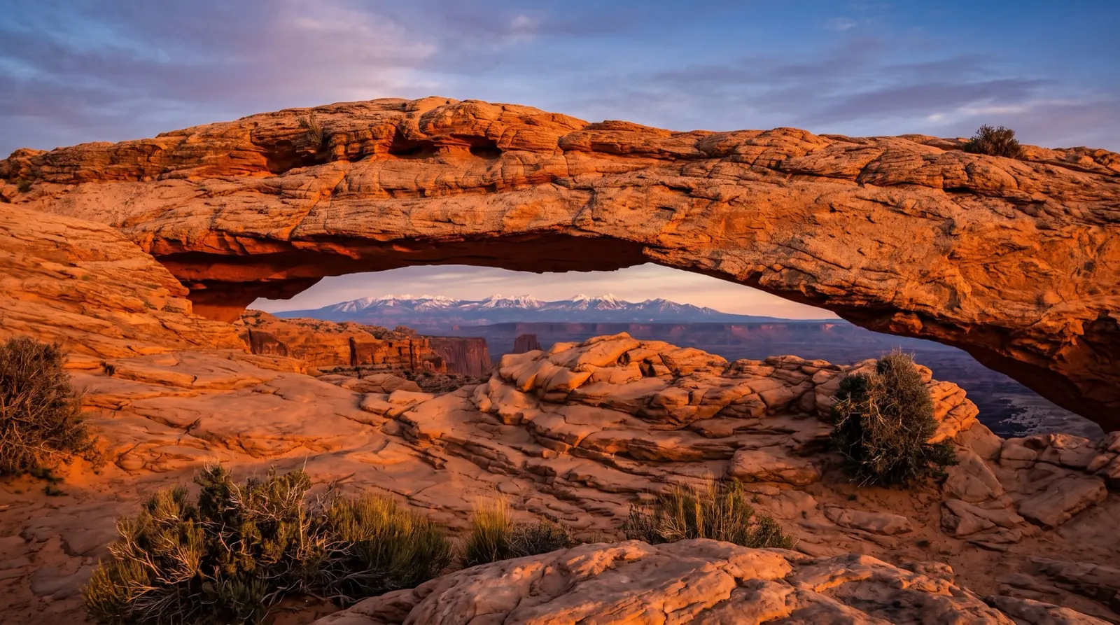 A red sandstone arch near Moab glowing orange at sunset with the La Sal mountains beyond